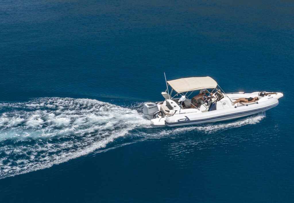 A white motorboat with a canopy speeds through the clear blue water near Dubrovnik, leaving a wake behind. Several people are seated, while one person relaxes at the front, ready to explore sea caves like the famous Blue Grotto.